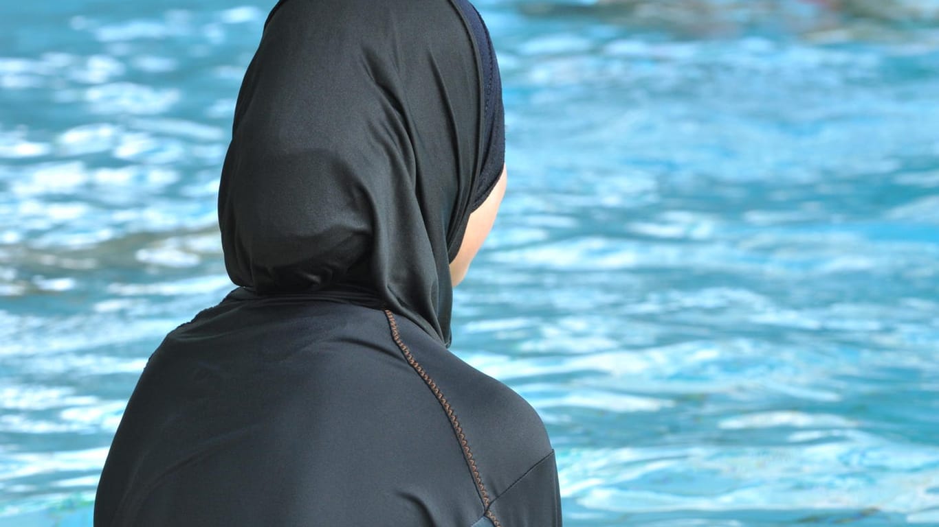 Eine muslimische Schülerin in einem Ganzkörper-Badeanzug (Burkini) am Rande eines Schwimmbeckens.