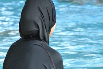 Eine muslimische Schülerin in einem Ganzkörper-Badeanzug (Burkini) am Rande eines Schwimmbeckens.