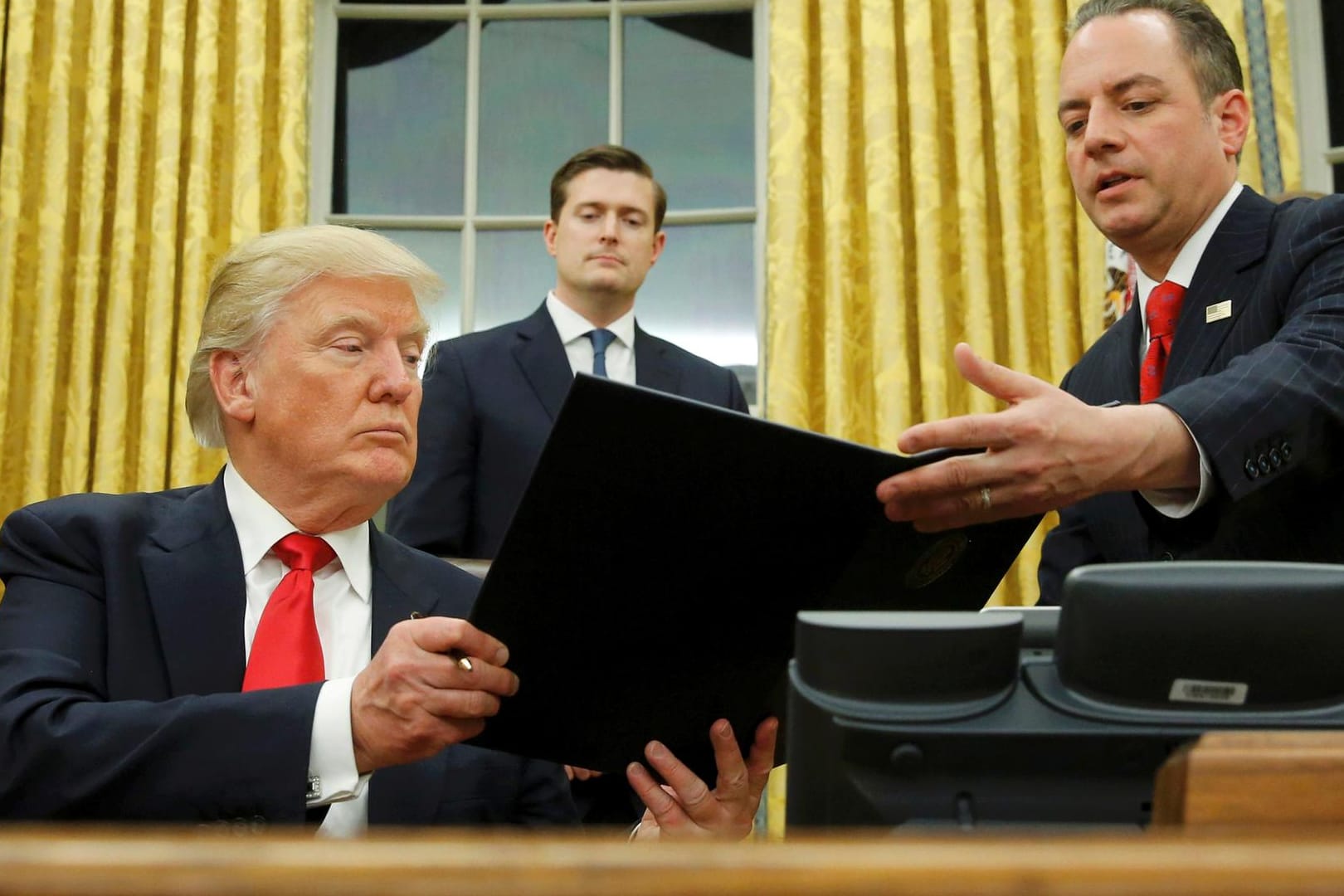 US-Präsident Donald Trump überreicht sein Dekret gegen "Obamacare" seinem Stabs-Chef Reince Priebus. Rob Porter (Mitte) guckt zu.