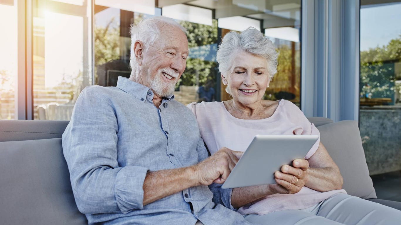Zwei Senioren sitzen auf der Terrasse und benutzen ein Tablet.
