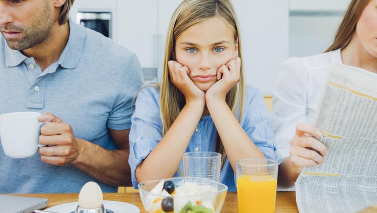Ein frustriertes Mädchen sitzt mit ihren Eltern am Frühstückstisch