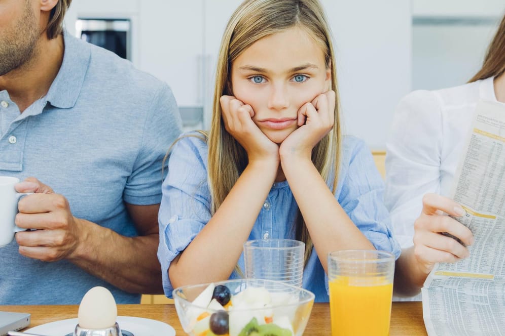 Ein frustriertes Mädchen sitzt mit ihren Eltern am Frühstückstisch