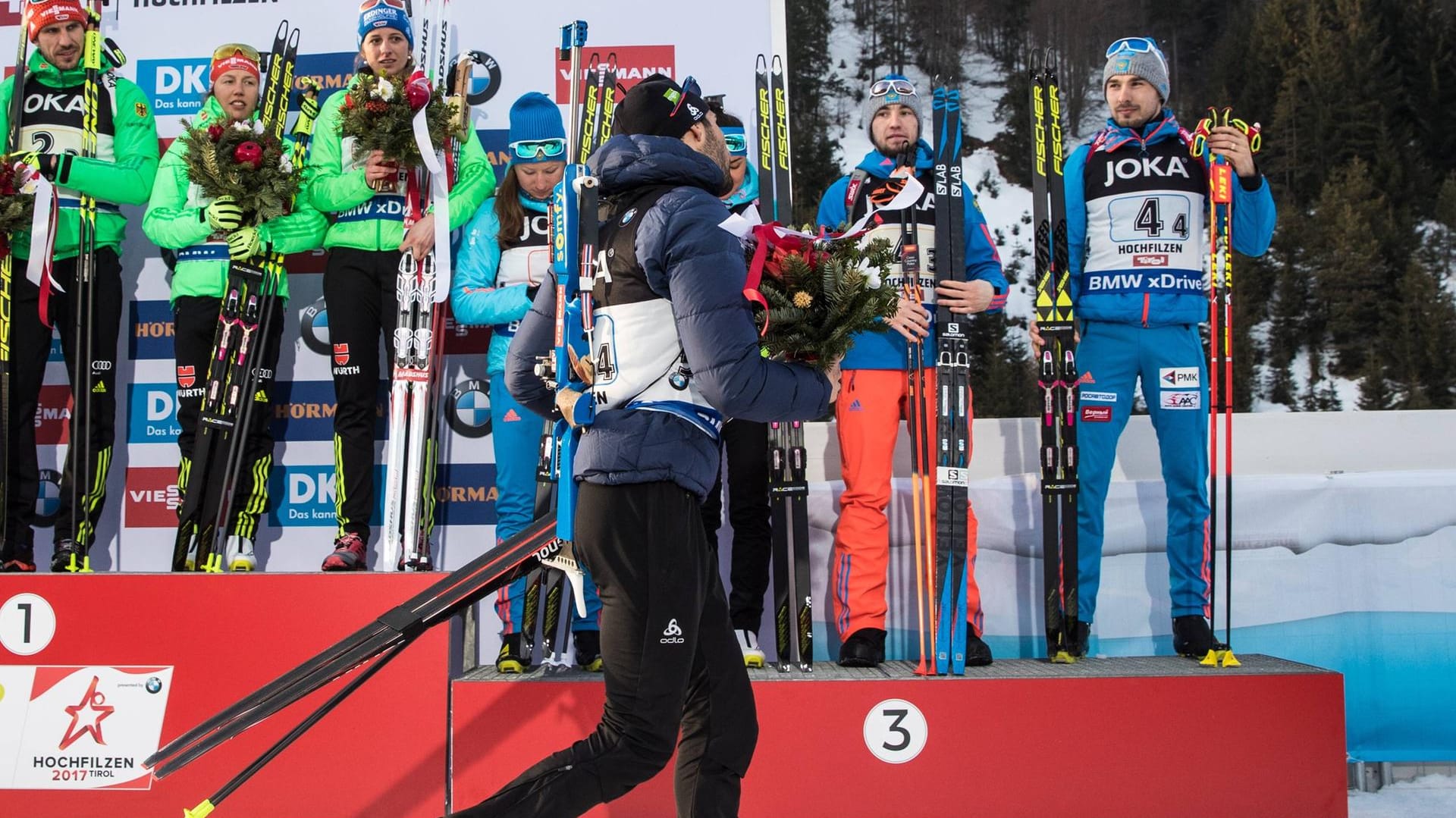 Vorzeitiger Abgang: Der Franzose Martin Fourcade (vorne) verließ die Siegerehrung aus Protest gegen das russische Team (im Hintergrund).