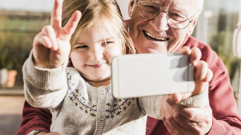 Großvater und Enkelin nehmen ein Selfie mit einem Smartpone auf.