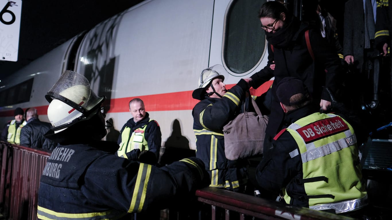 Feuerwehrleute und Bahn-Mitarbeiter helfen Bahnreisenden aus dem ICE, auf den eine Oberleitung gefallen war.