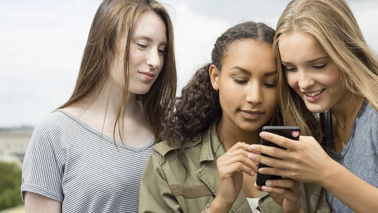 Drei jugendliche Mädchen gucken auf ein Handy.