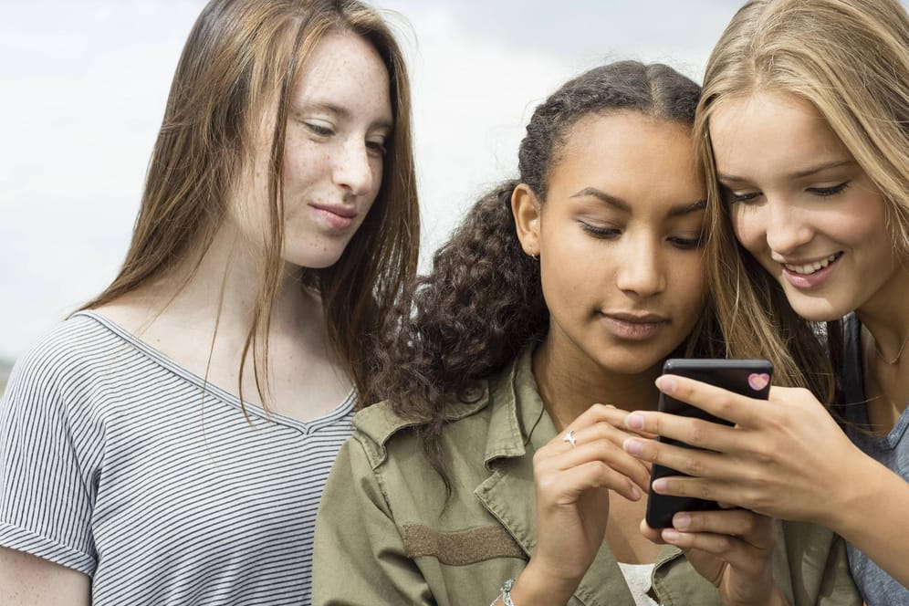 Drei jugendliche Mädchen gucken auf ein Handy.