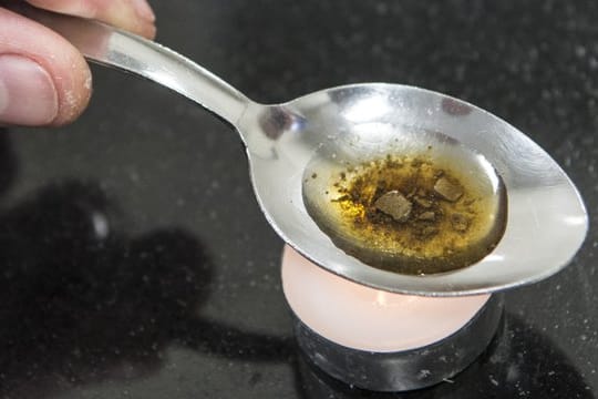 Ein Mann "kocht" sich auf einem Löffel die Dosis für einen Schuss Heroin.