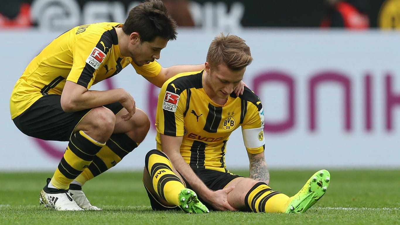 Dortmunds Marco Reus sitzt verletzt auf dem Rasen und wird danach ausgewechselt. Neben ihm Raphael Guerreiro (li).