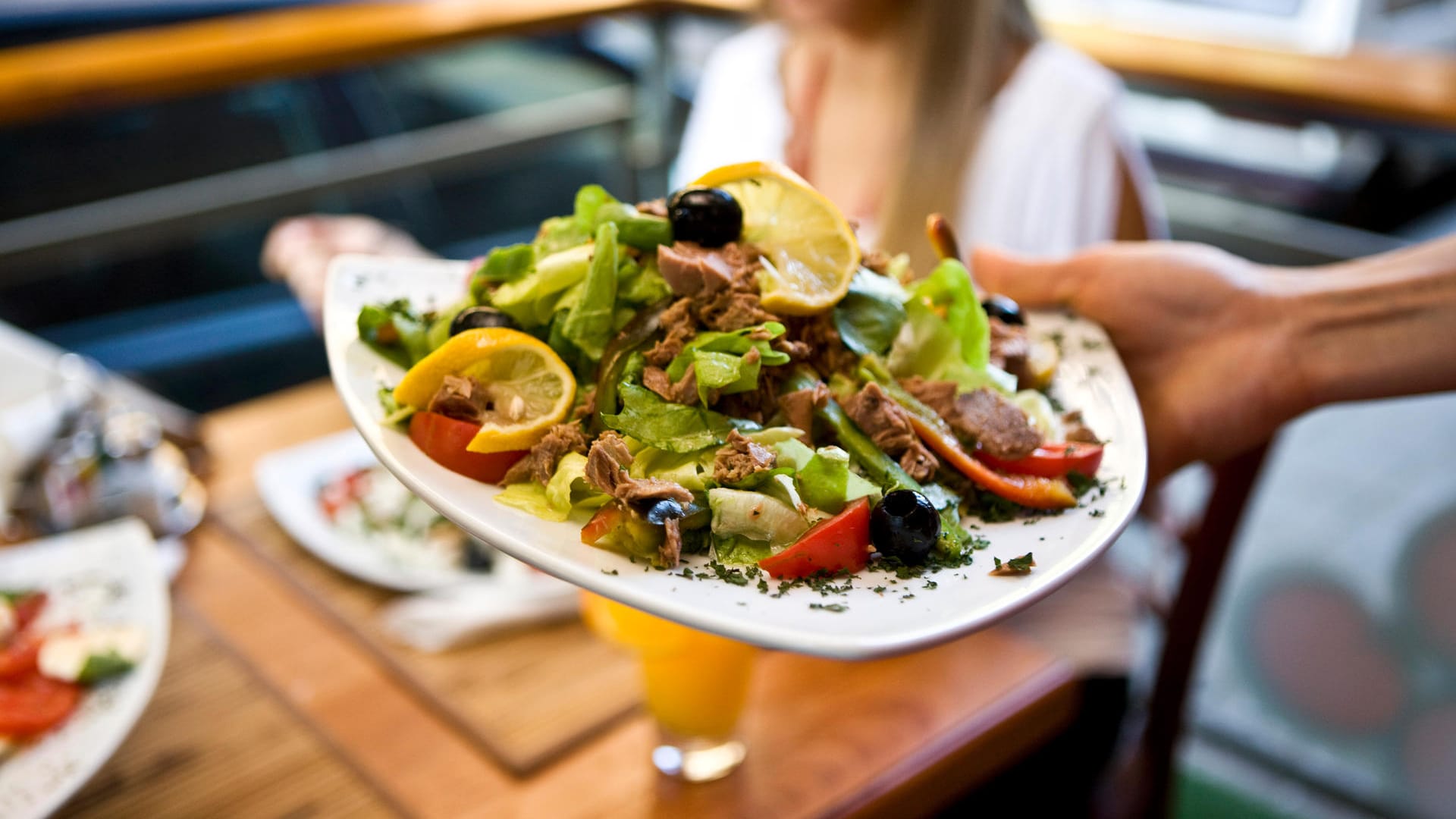 Einer Frau wird ein mediterraner Salat serviert.