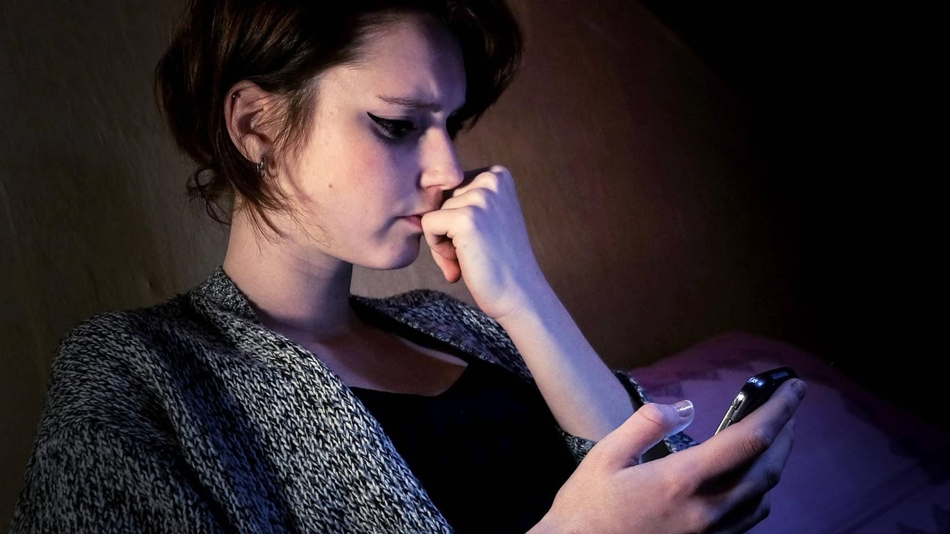 Eine junge Frau schaut unzufrieden auf ihr Smartphone.