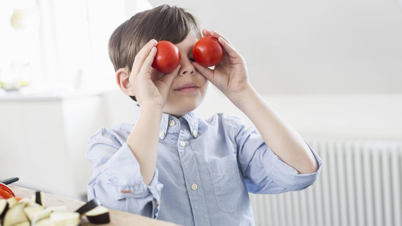 Ein Junge hält sich zwei Tomaten vor die Augen.