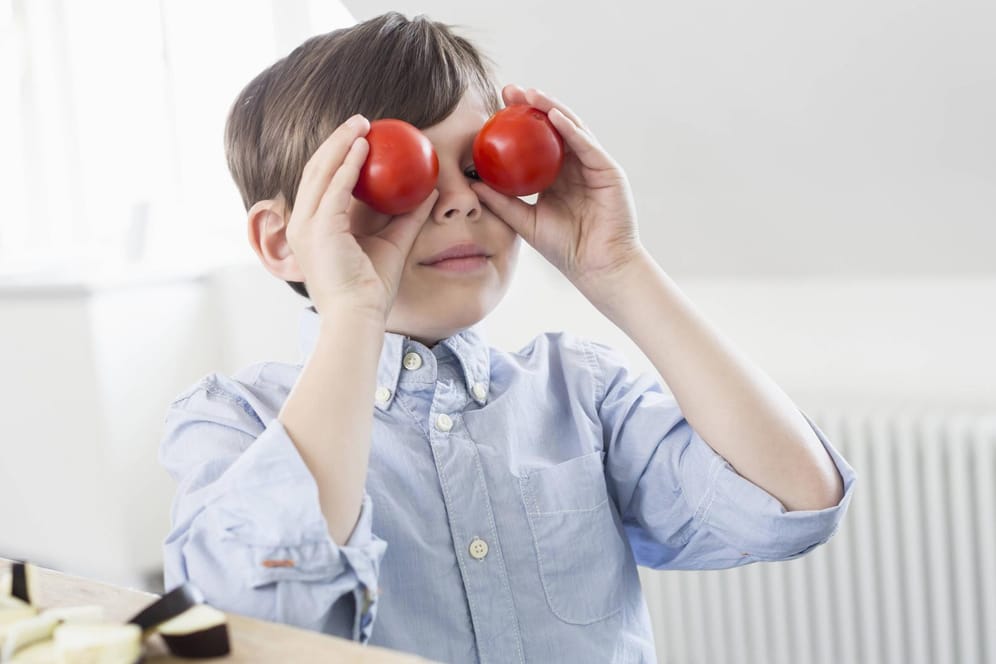 Ein Junge hält sich zwei Tomaten vor die Augen.