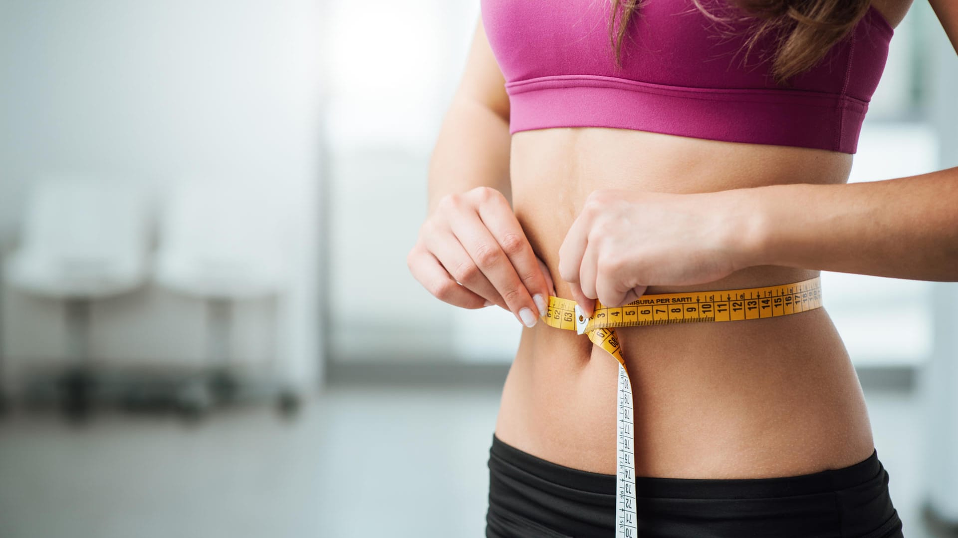 Eine Frau hält sich ein Maßband um den Bauch.