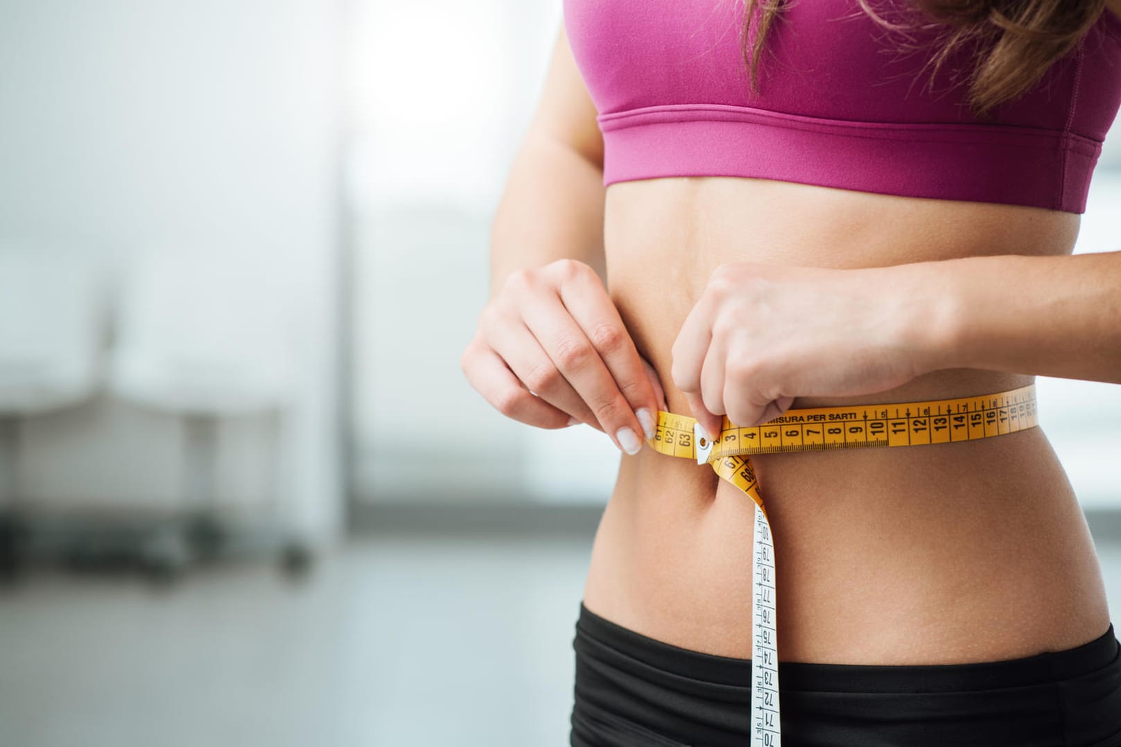 Eine Frau hält sich ein Maßband um den Bauch.