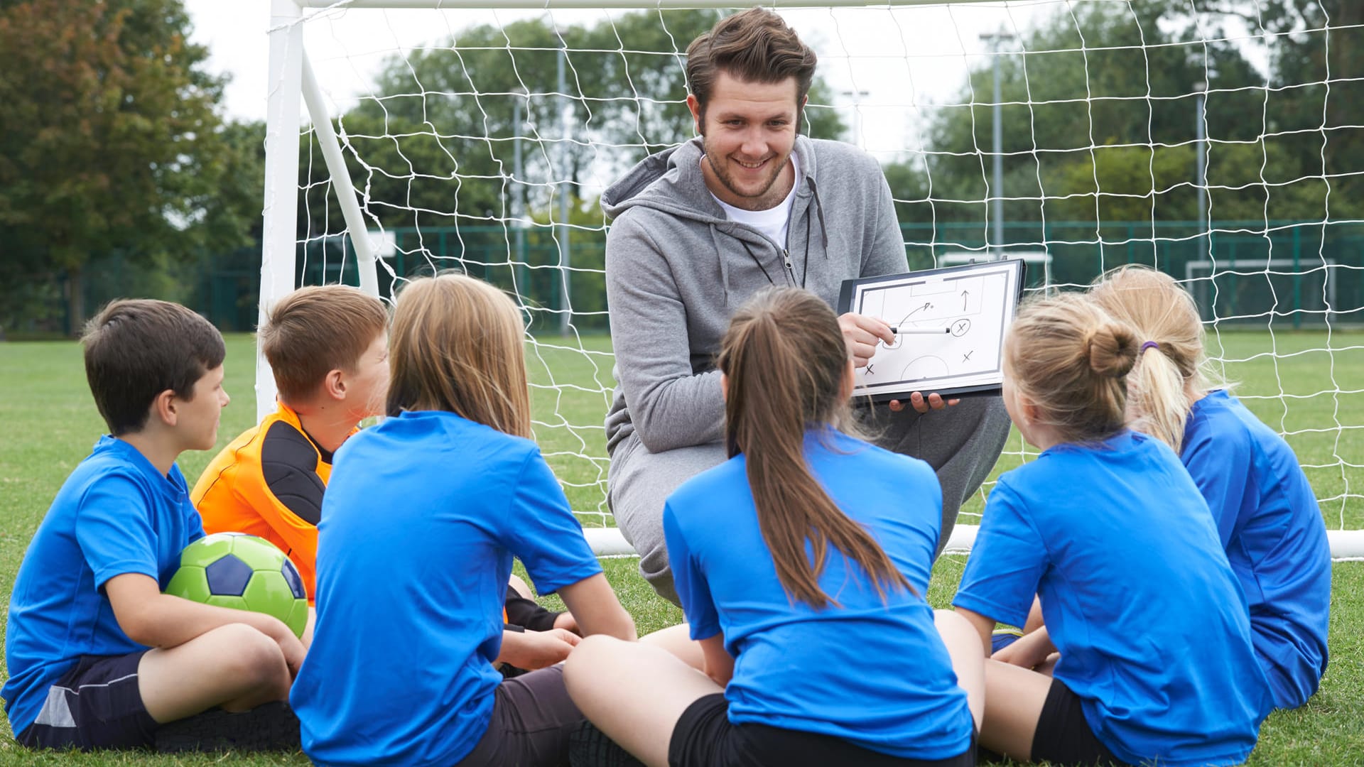 Ein Trainer gibt Kindern Tipps beim Fußballspielen