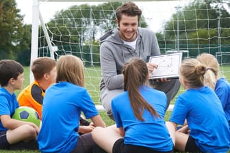 Ein Trainer gibt Kindern Tipps beim Fußballspielen