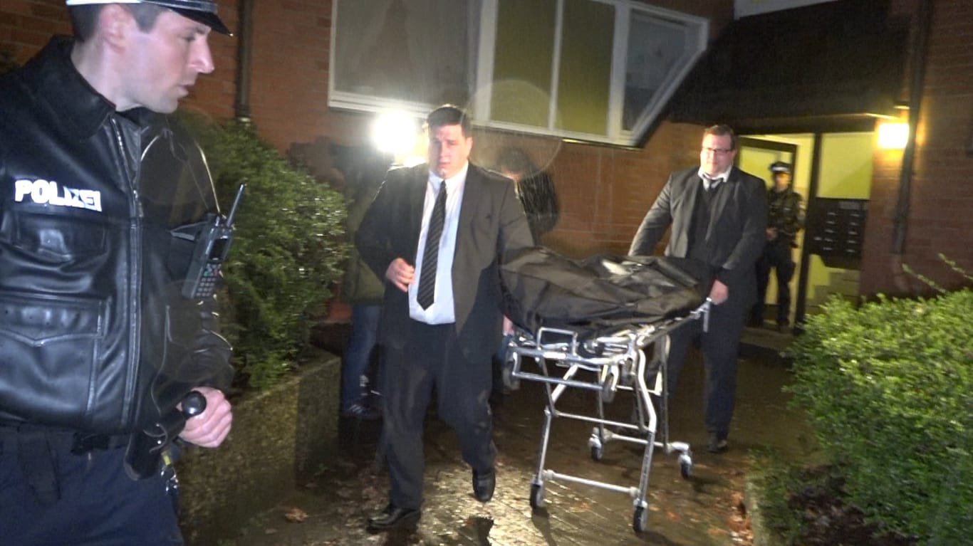 Mitarbeiter eines Bestattungsunternehmens sowie ein Polizist transportieren die Leichen aus dem Haus.