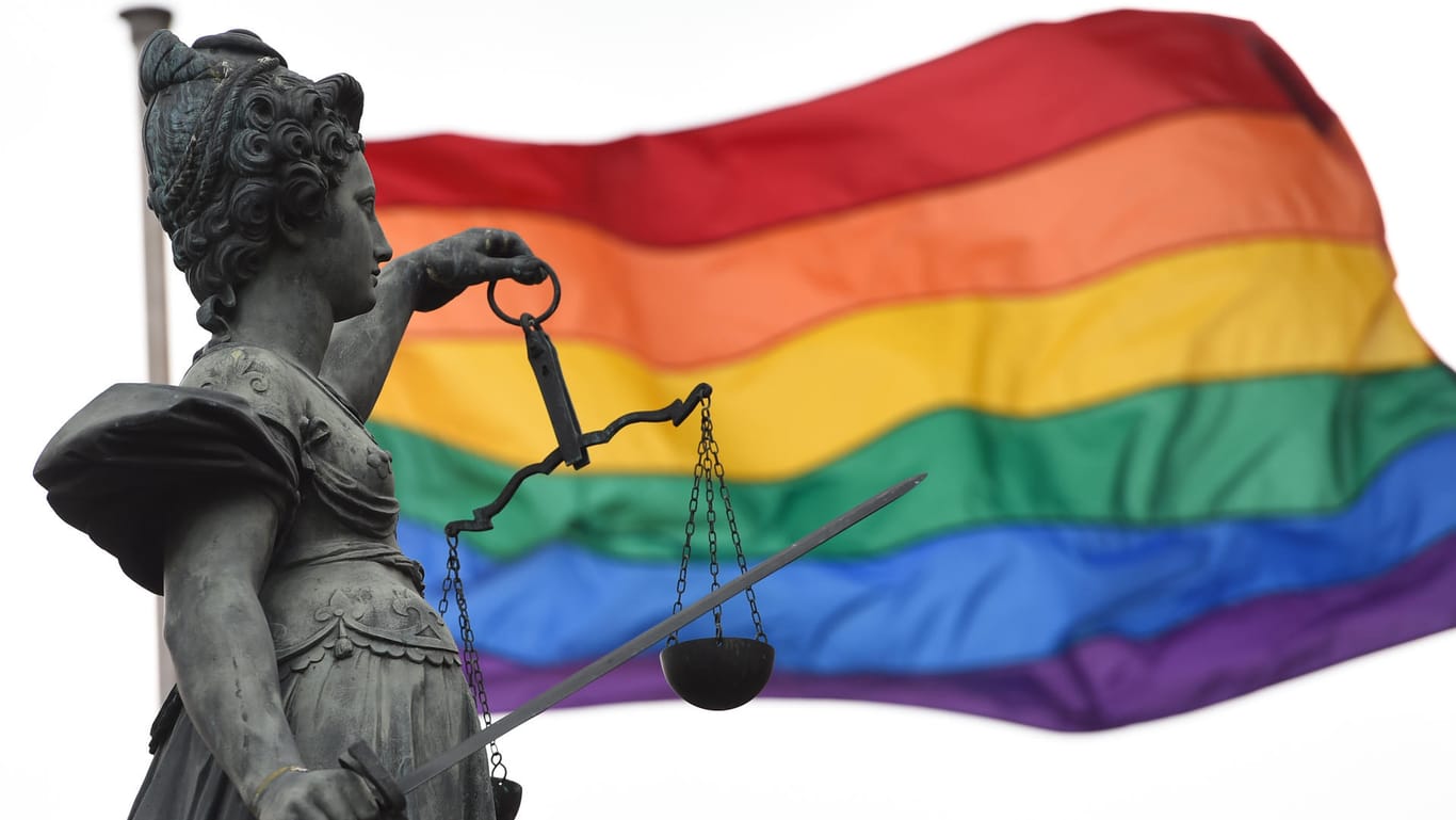Justitia vor der Regenbogenfahne, dem Symbol der Lesben und Schwulen.