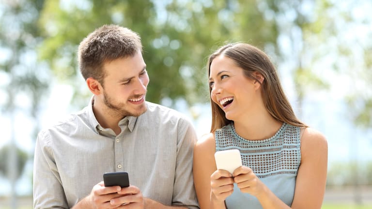 Eine Frau und ein Mann haben Handys in der Hand und lächeln sich an.