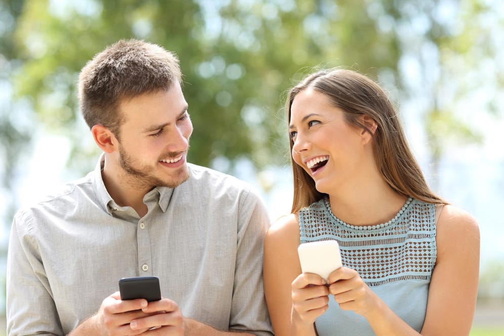Eine Frau und ein Mann haben Handys in der Hand und lächeln sich an.