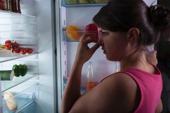 Eine Frau steht vor einem Kühlschrank und hält sich die Nase zu