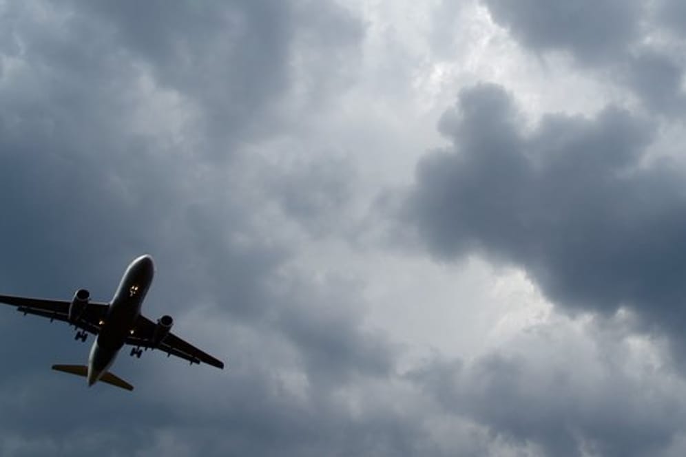 Gewitterwolken türmen sich über einem landenden Flugzeug auf.