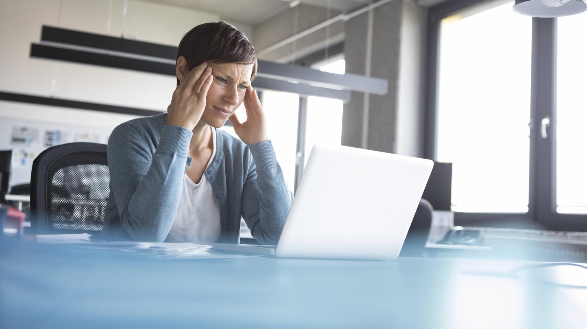 Businesswoman in office with head in hands using laptop model released Symbolfoto property released