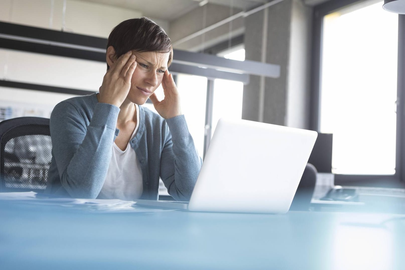 Businesswoman in office with head in hands using laptop model released Symbolfoto property released