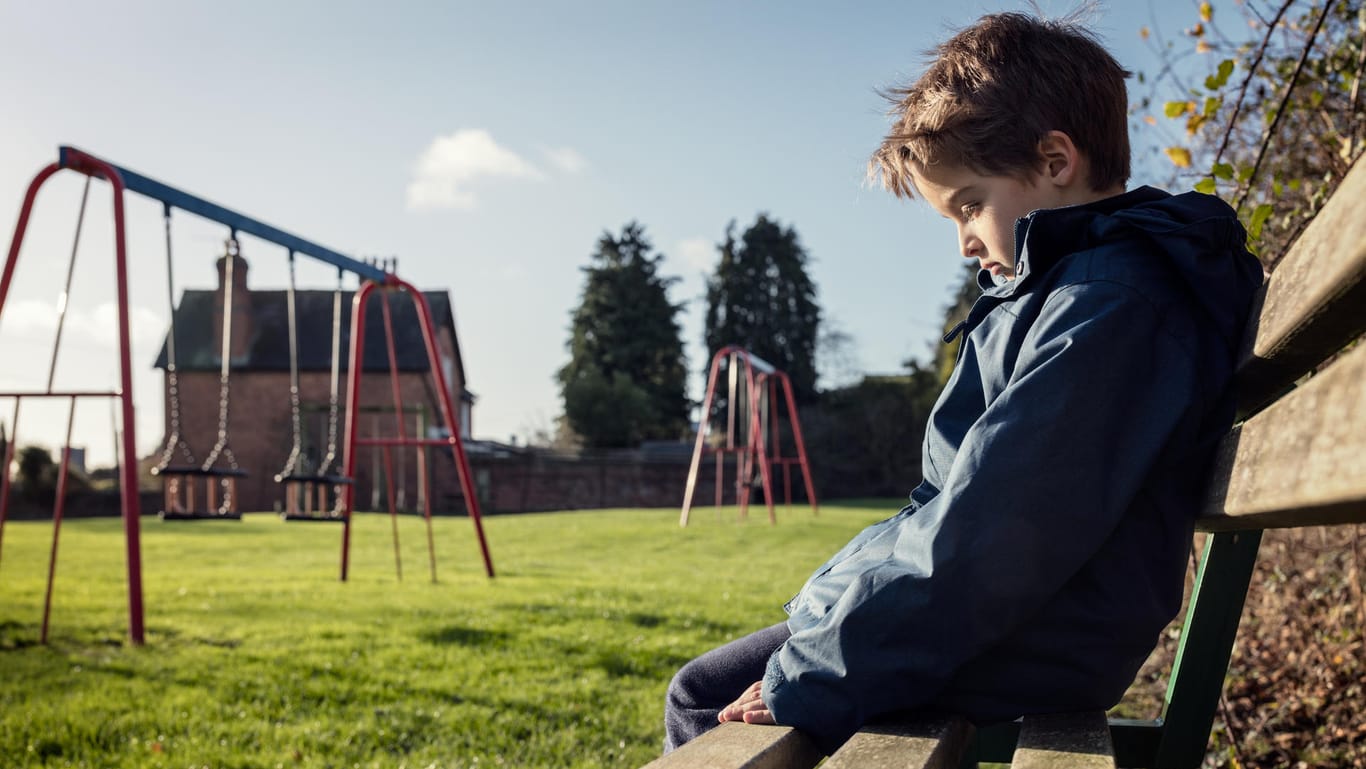 Eine Junge sitzt alleine auf dem Spielplatz