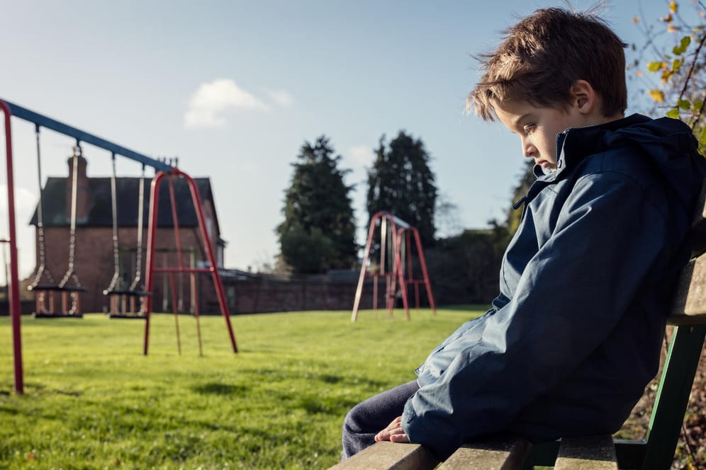 Eine Junge sitzt alleine auf dem Spielplatz