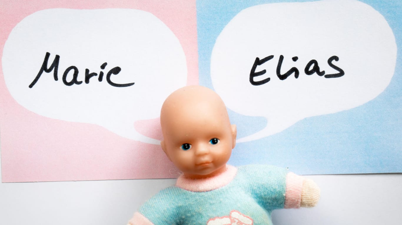 Eine Puppe liegt vor zwei Zetteln mit Sprechblasen, in denen die Namen "Marie" und "Elias" stehen.