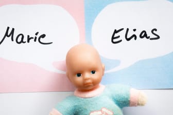 Eine Puppe liegt vor zwei Zetteln mit Sprechblasen, in denen die Namen "Marie" und "Elias" stehen.