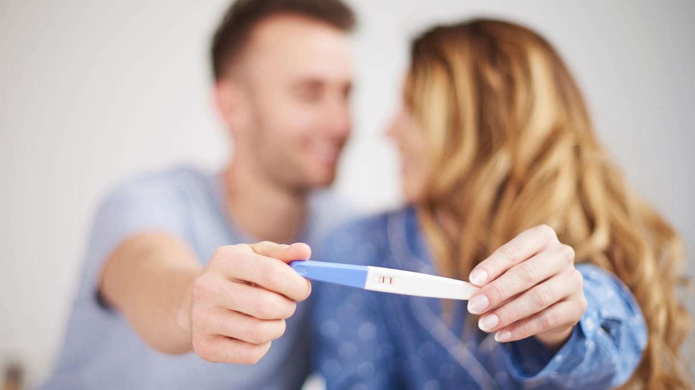 Ein junges Paar hält einen Schwangerschaftstest in die Kamera.