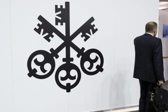 Mann mit Koffer vor einem Logo der UBS-Bank (Symbolbild).