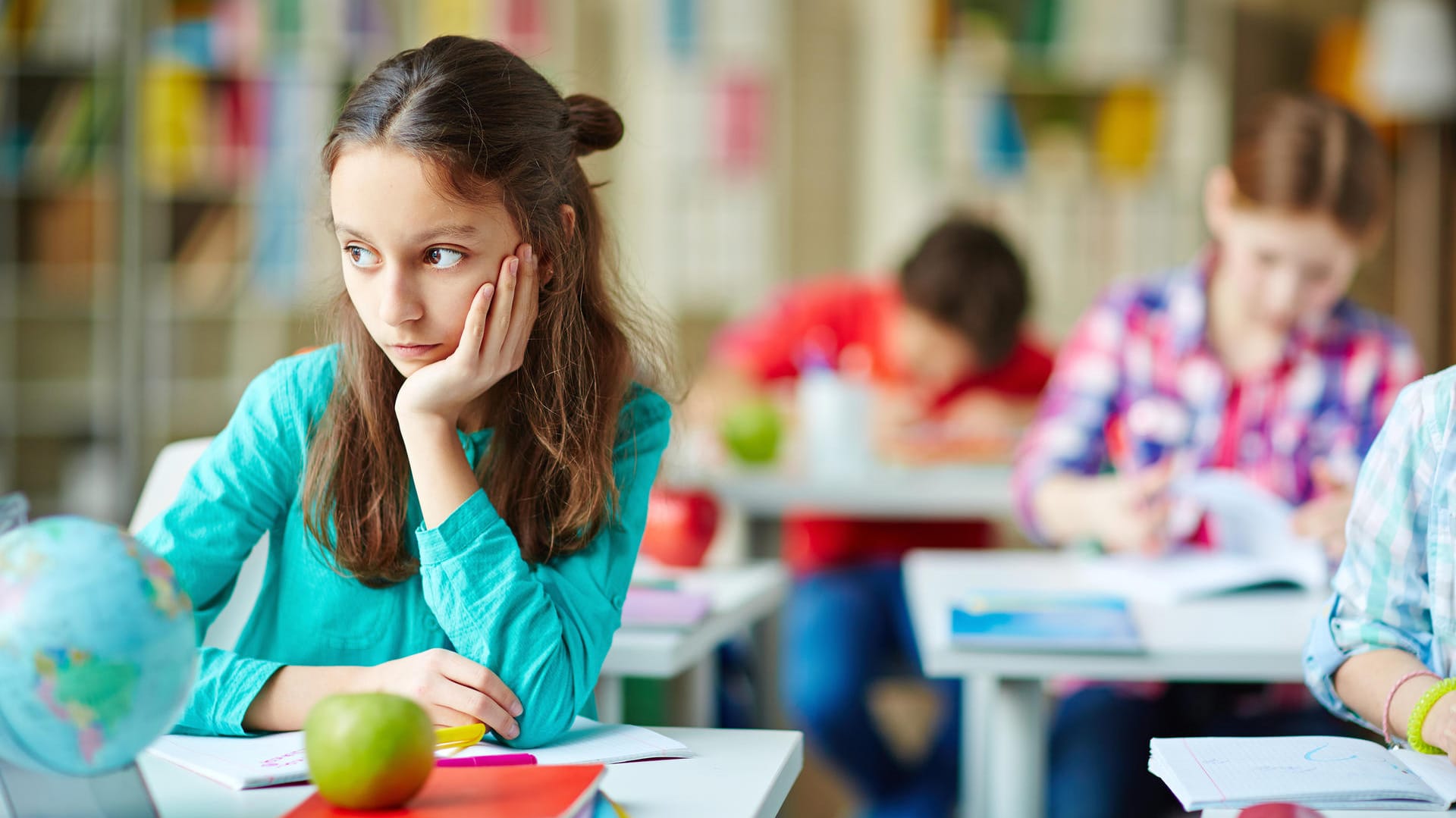 Ein Mädchen sitzt nachdenklich an seiner Schulbank.