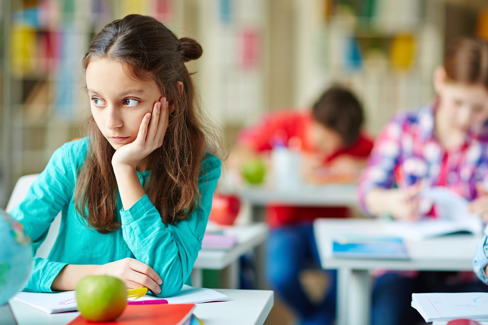 Ein Mädchen sitzt nachdenklich an seiner Schulbank.