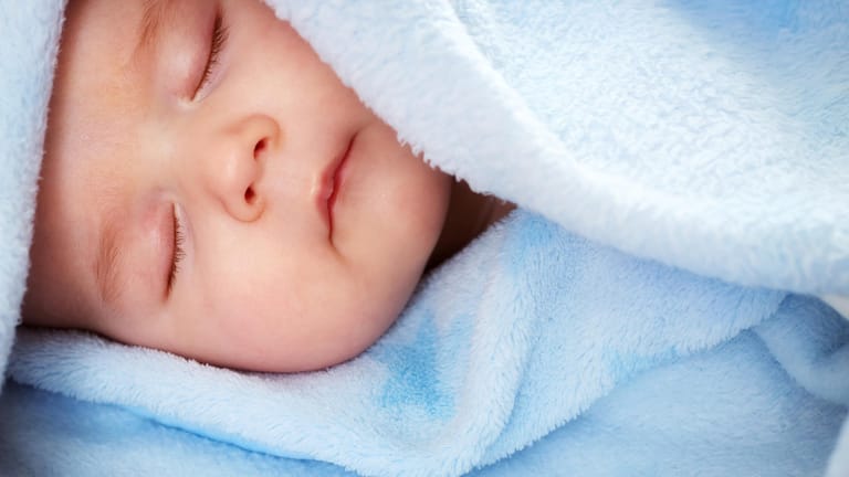 Ein Baby liegt in einer blauen Kuscheldecke.