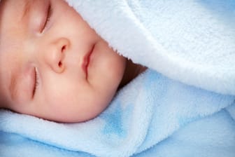 Ein Baby liegt in einer blauen Kuscheldecke.