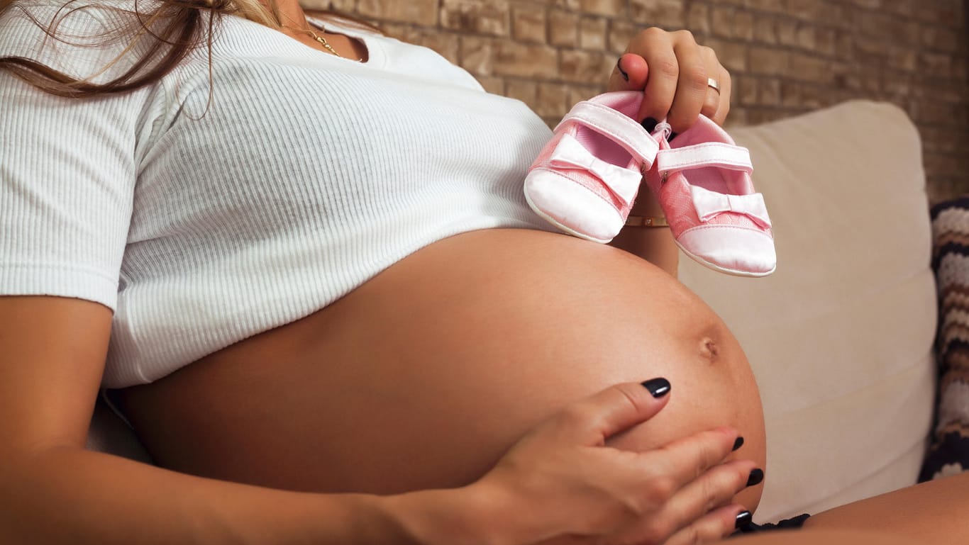 Eine Schwangere hält Babyschuhe an ihren Bauch.