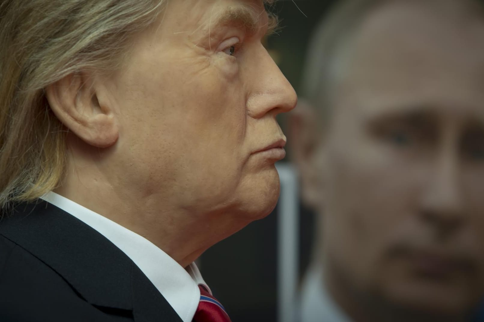 Eine Wachsfigur von Donald Trump vor einem Foto Putins.