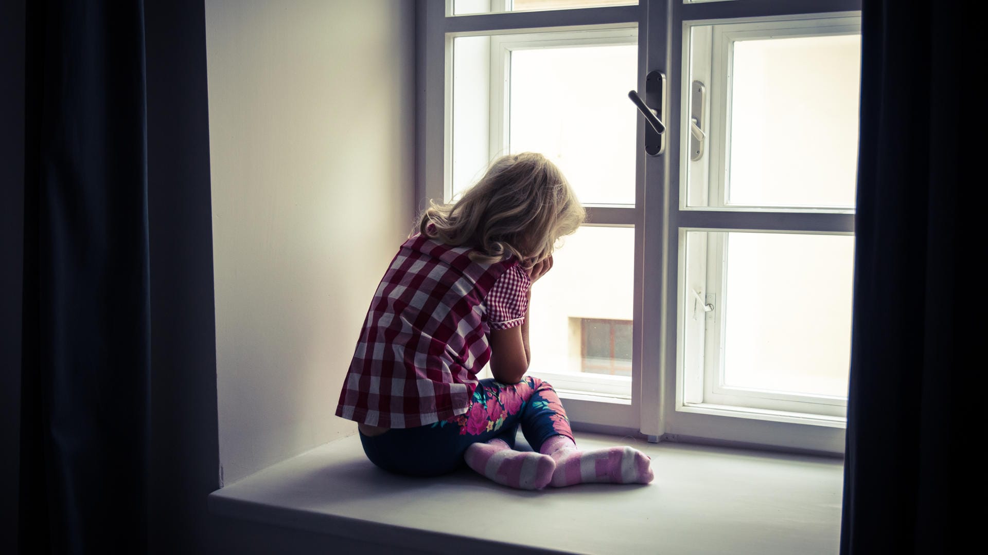 Ein Mädchen sitzt vor einem Fenster: Gewalt gegen Kinder lässt sich nicht auf Altersgruppen oder Schichten zurückführen.