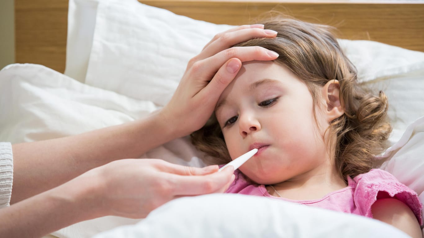 Ein Mädchen liegt mit Fieberthermometer im Mund im Bett