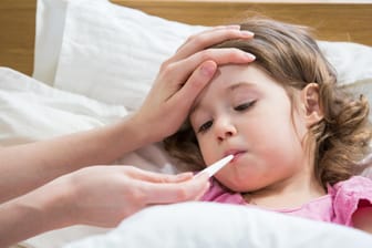 Ein Mädchen liegt mit Fieberthermometer im Mund im Bett