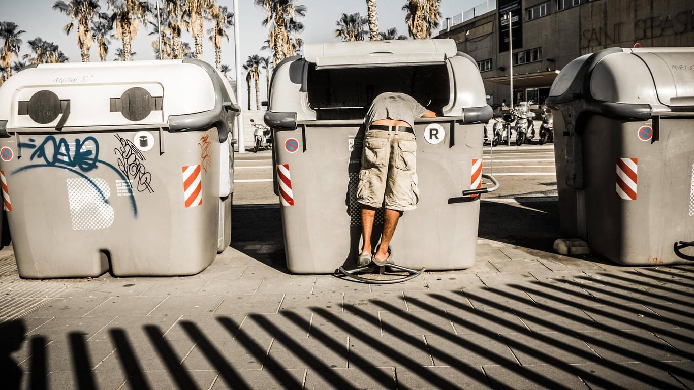 Eine Person durchsucht eine Mülltonne in Barcelona.