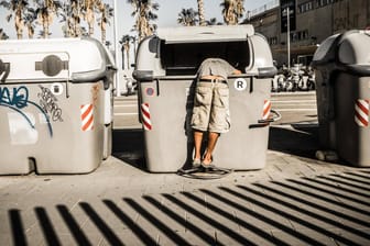 Eine Person durchsucht eine Mülltonne in Barcelona.