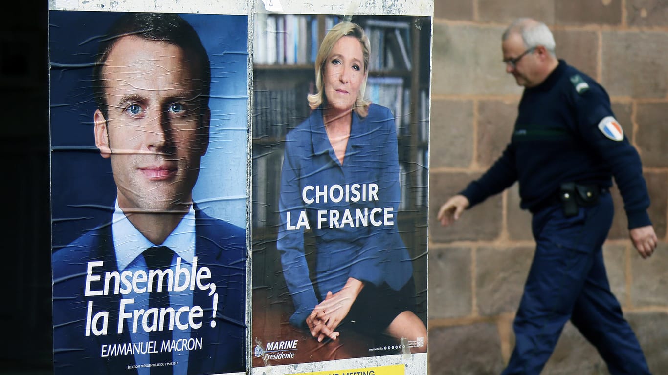 Ein Polizist geht an den Wahlplakaten von Emmanuel Macron (l) und Marine Le Pen (r) vorbei.