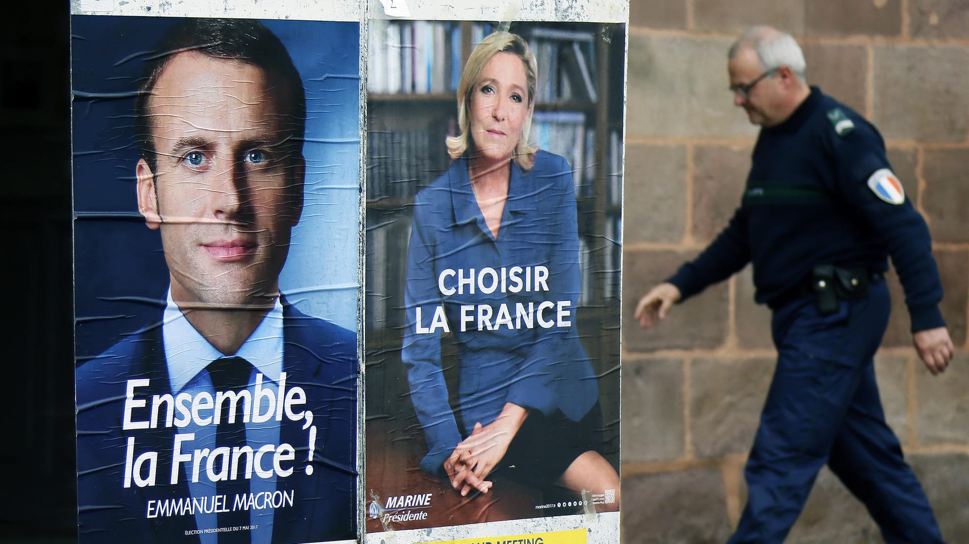 Ein Polizist geht an den Wahlplakaten von Emmanuel Macron (l) und Marine Le Pen (r) vorbei. Ein Polizist geht an den Wahlplakaten von Emmanuel Macron (l) und Marine Le Pen (r) vorbei.