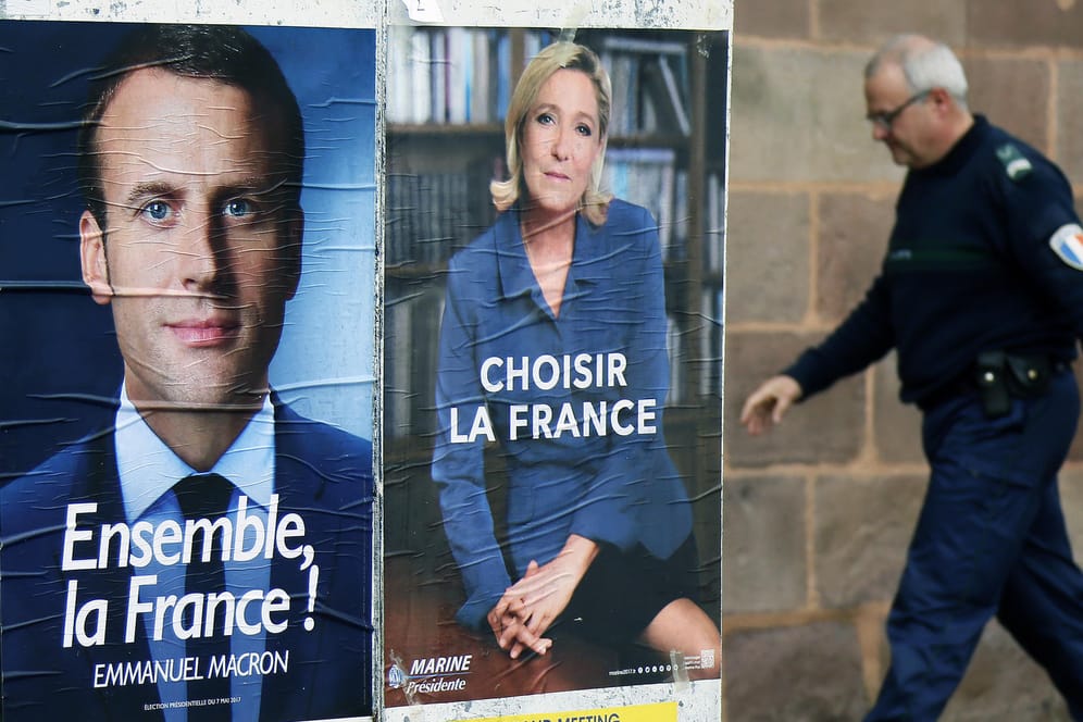 Ein Polizist geht an den Wahlplakaten von Emmanuel Macron (l) und Marine Le Pen (r) vorbei.