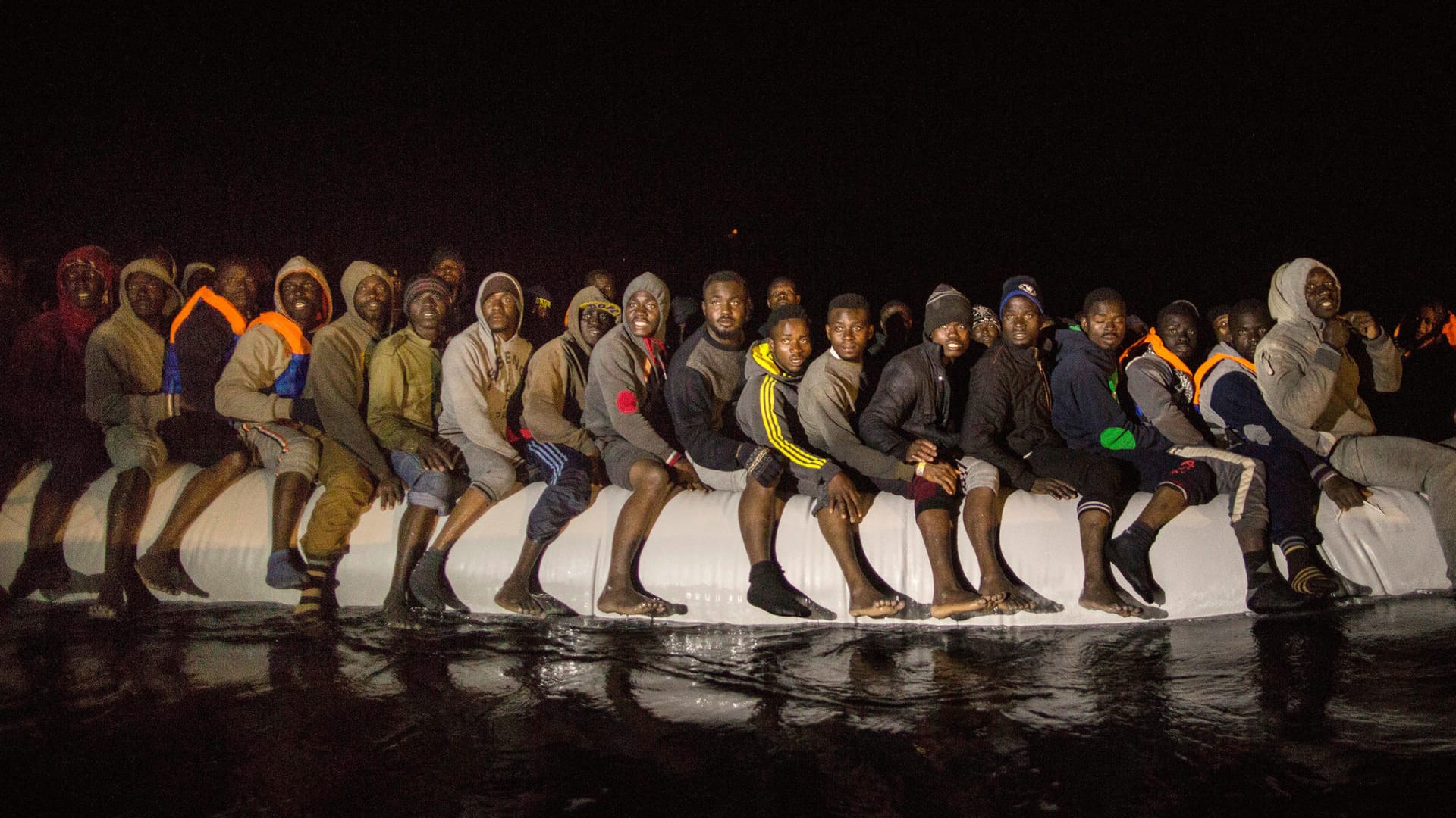 Flüchtlinge aus verschiedenen afrikanischen Staaten sitzen am frühen Morgen in einem überfüllten Schlauchboot auf dem Mittelmeer. Flüchtlinge aus verschiedenen afrikanischen Staaten sitzen am frühen Morgen in einem überfüllten Schlauchboot auf dem Mittelmeer.